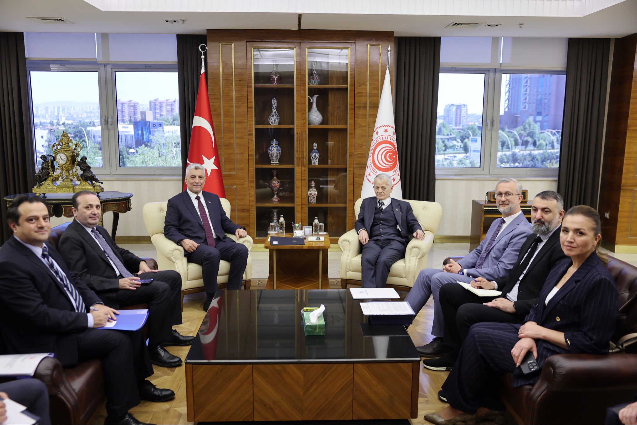 Ticaret Bakanlığı logolu resmi bir salonda, Türk bayrağı önünde iki ana yetkilinin ve heyetlerinin karşılıklı oturduğu toplantı anı.